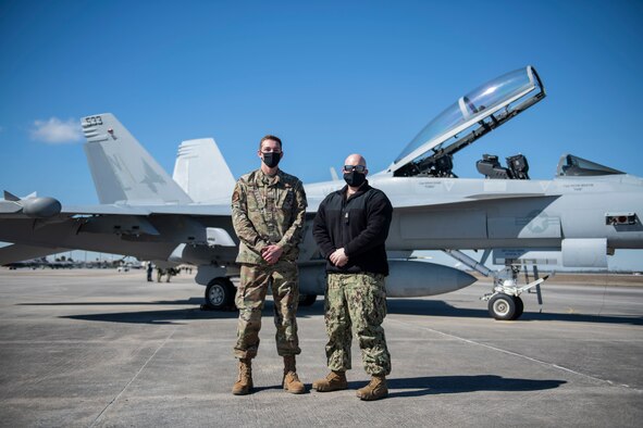 Two uniformed men stand in front of a EA-18G Growler aircraft.
