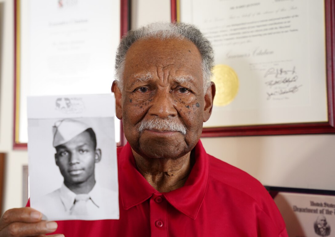 A veteran holds up a World War II-era photo of himself.