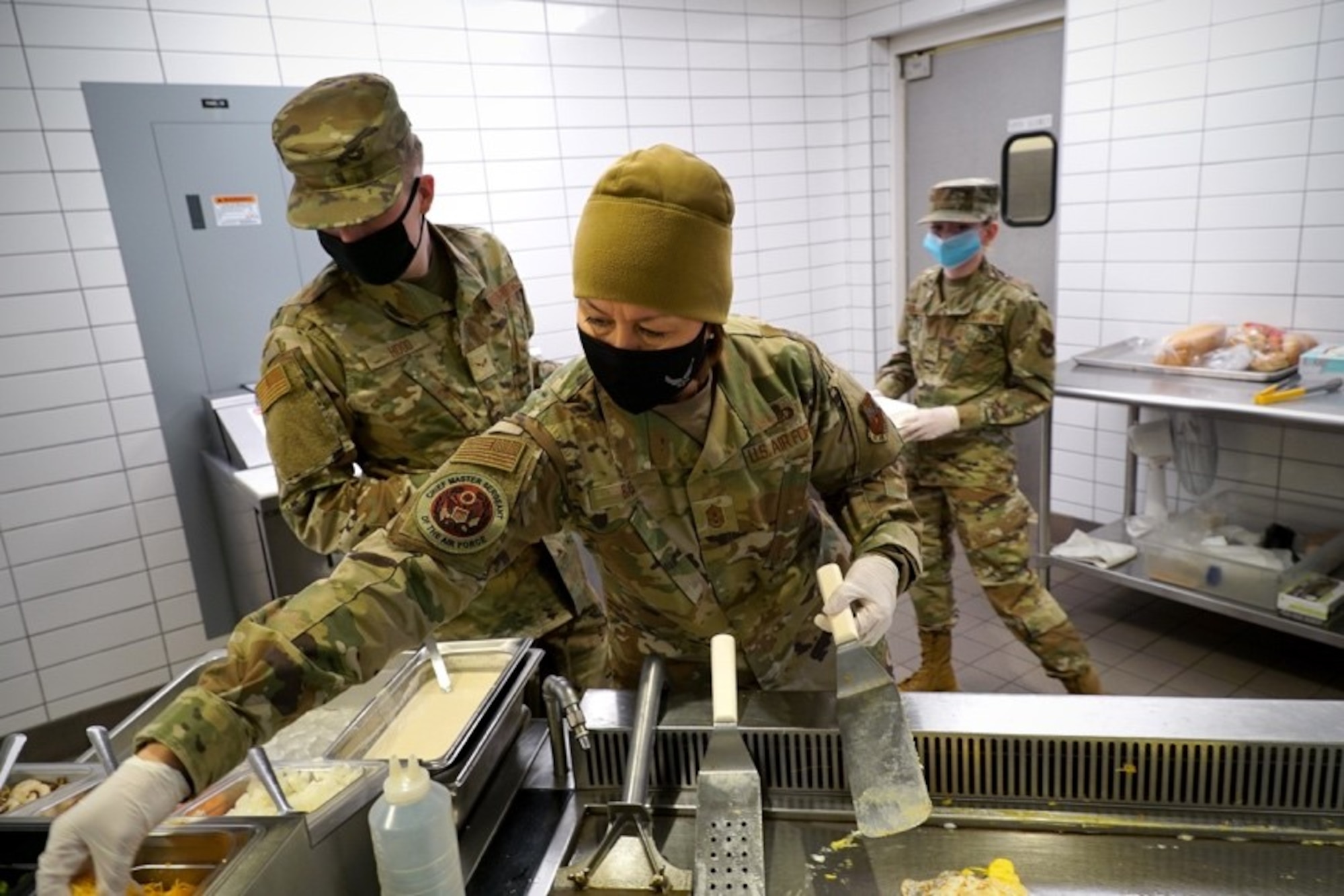 Chief Master Sergeant of the Air Force stands over a grill while preparing an omelet next to Airman 1st Class Samuel Hood.