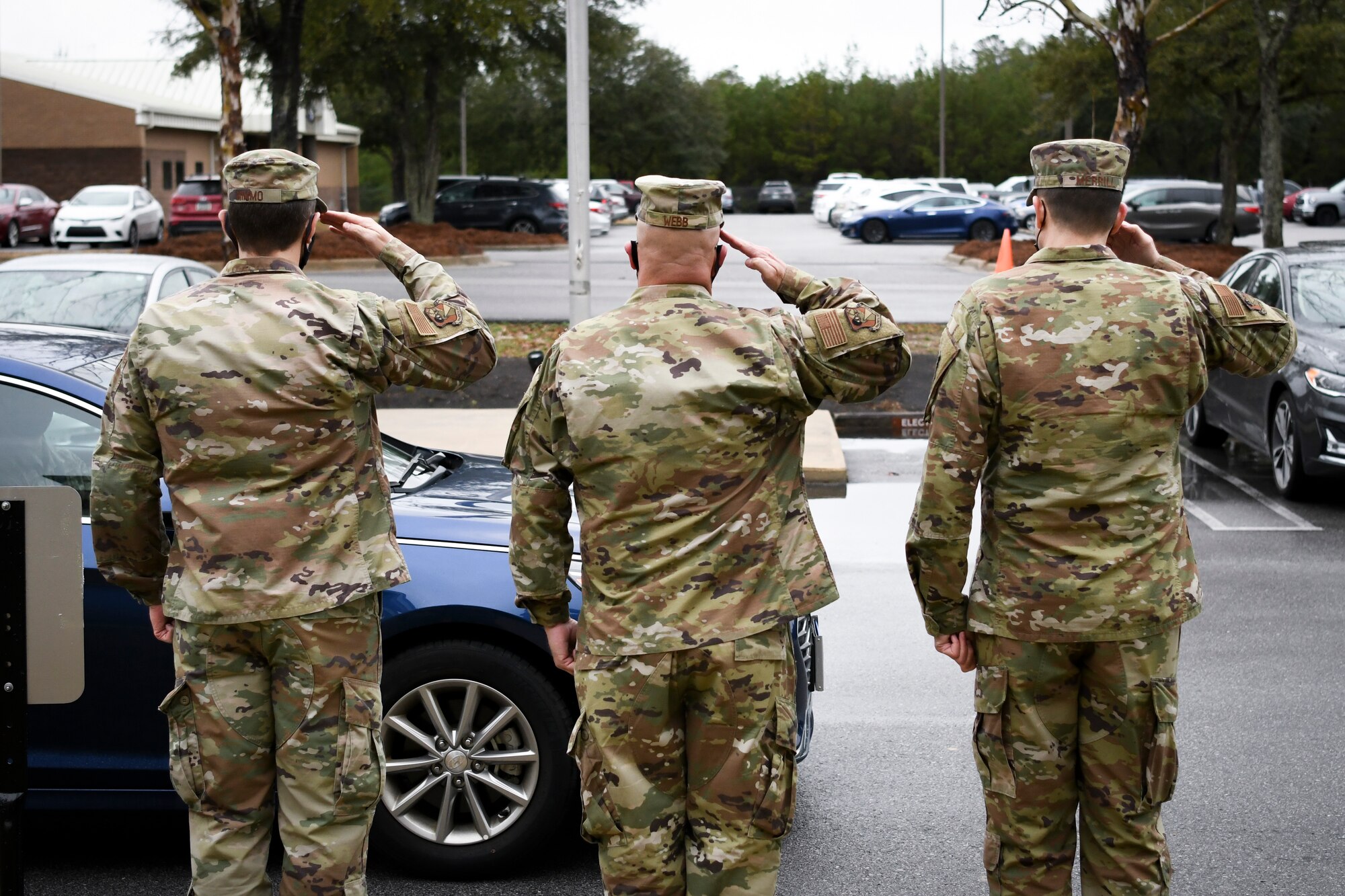 Photo of three Airmen saluting a vehicle