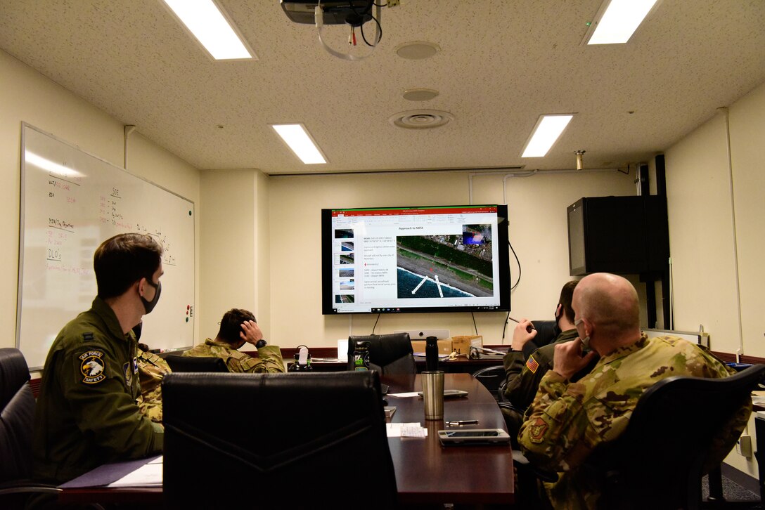 Airmen sit in a conference room observing a powerpoint slide