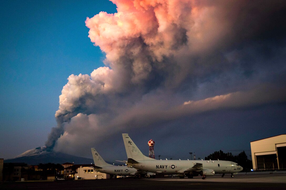 Aircraft sit on tarmac while a volcano lets out steam in the background.