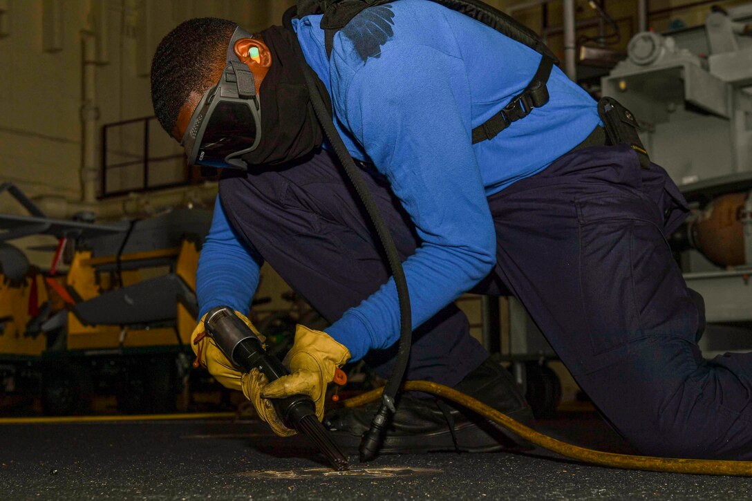 An airman uses a needle gun on a ship.