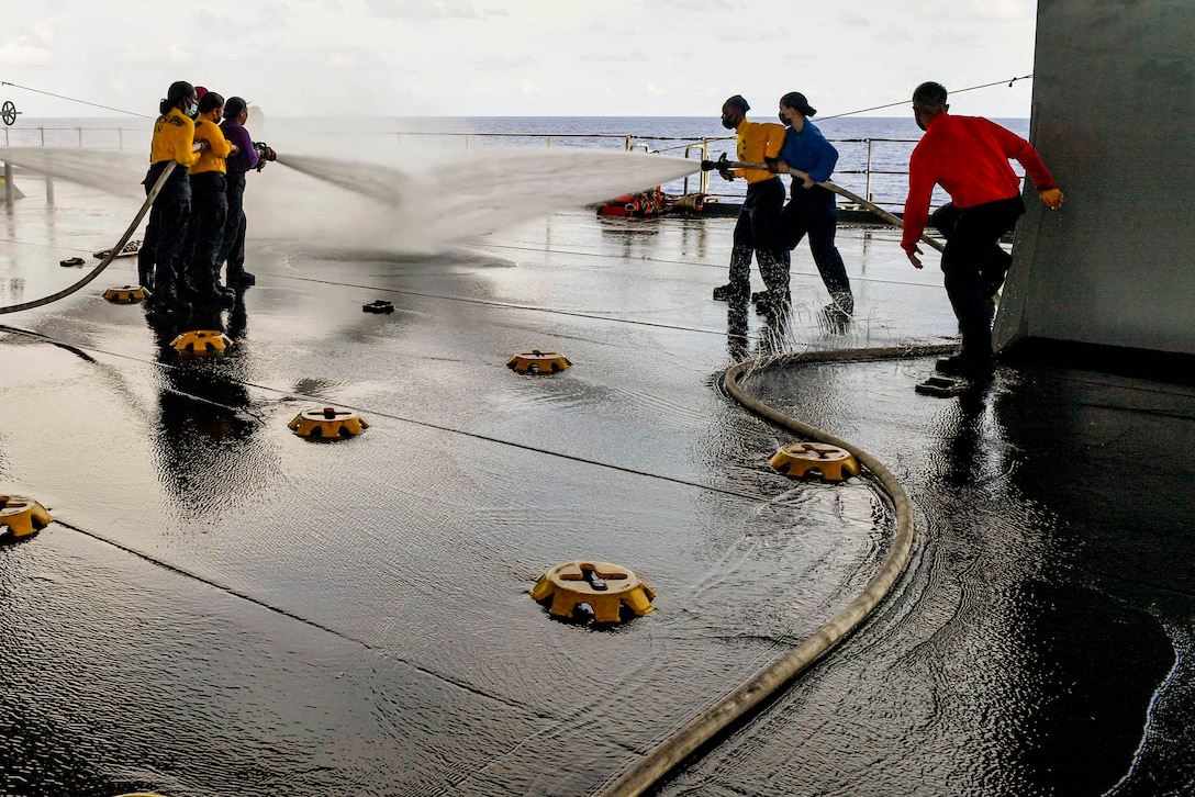 Sailors hold water hoses on a ship.