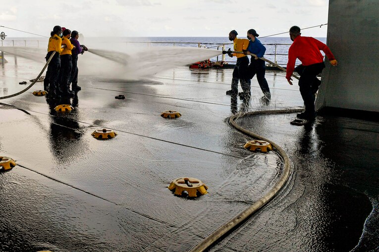Sailors hold water hoses on a ship.