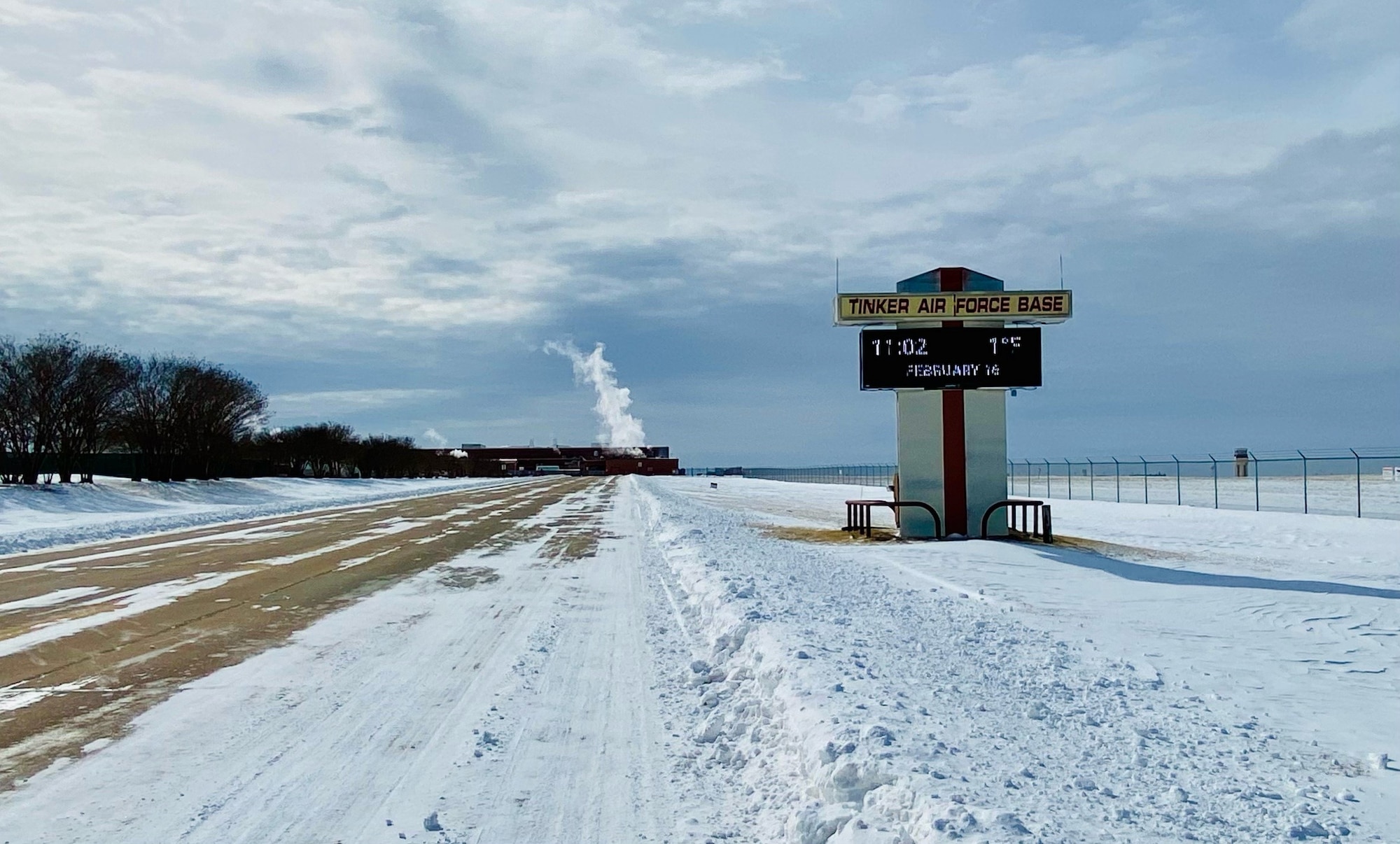 A snow-plowed road with an LED sign to the right.