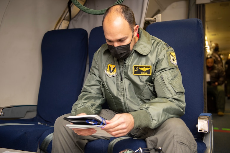 Photo shows man sitting in aircraft seat looking at manual.