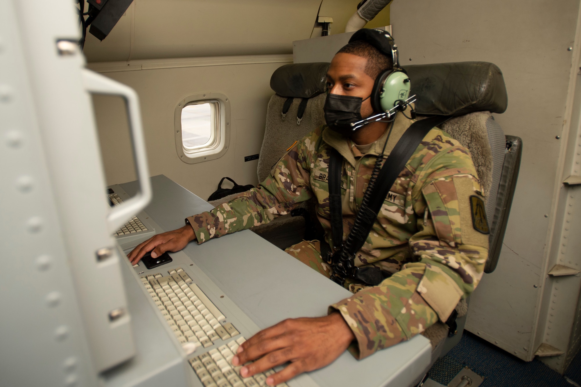 Photo shows man sitting on aircraft in front of a monitor.