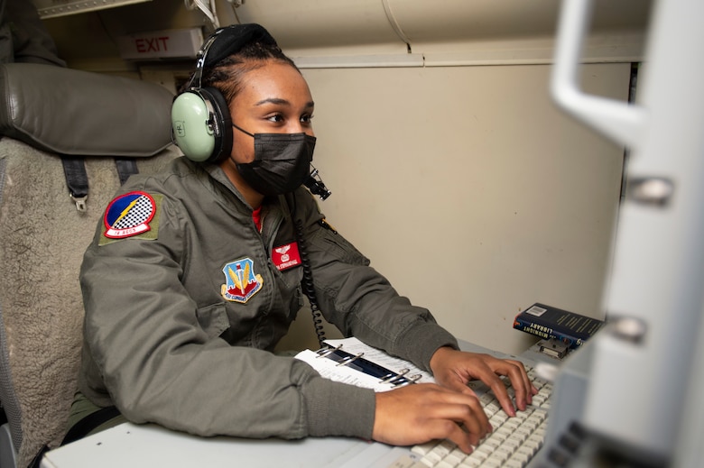 Photo shows woman sitting on aircraft typing on a keyboard while looking at a monitor.