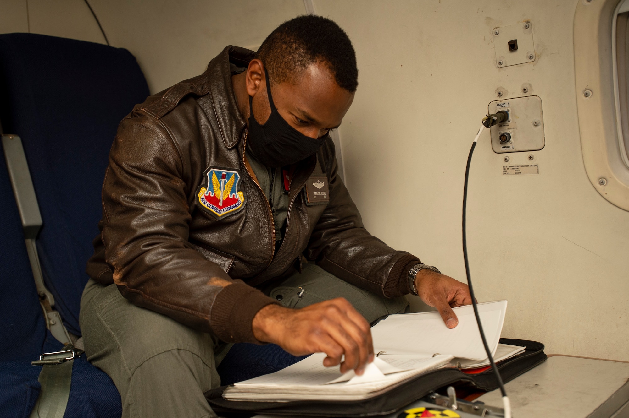 Photo shows man sitting in aircraft seat looking at a manual.