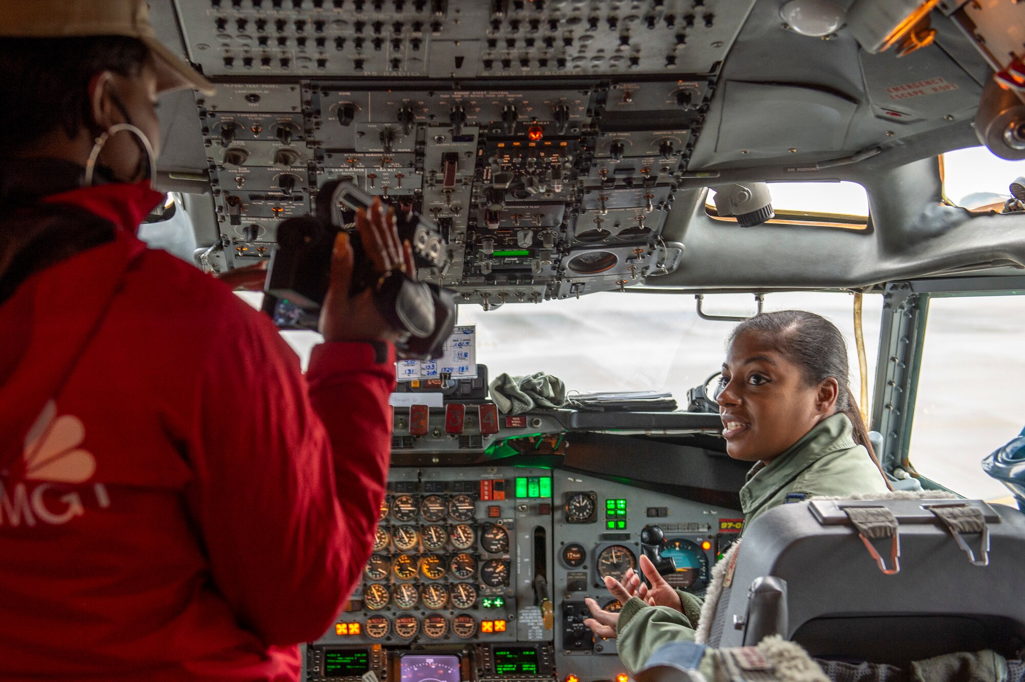 Photo shows woman sitting in cockpit of aircraft being interviewed on camera.
