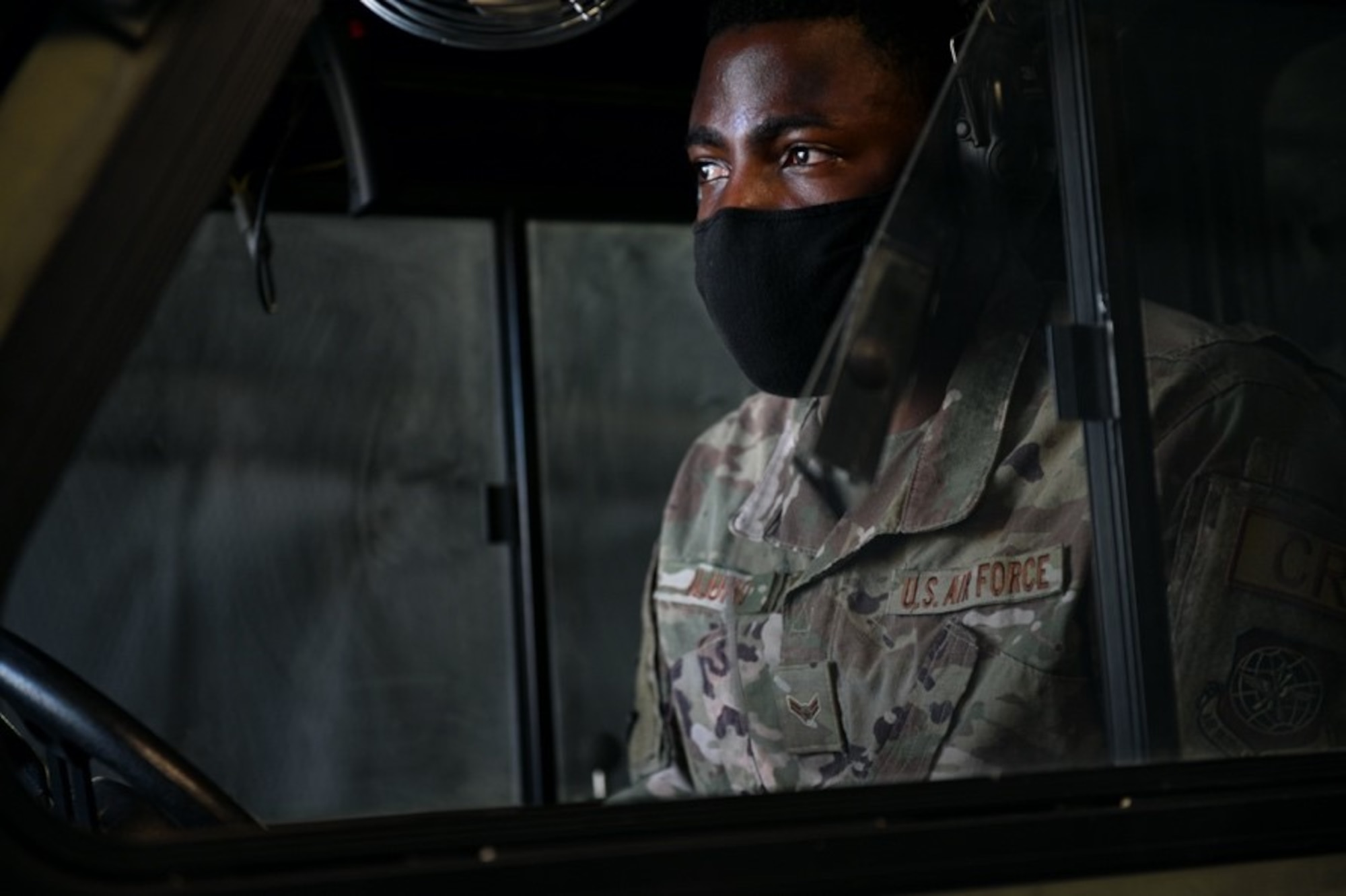 A military member in uniform and mask looks off screen