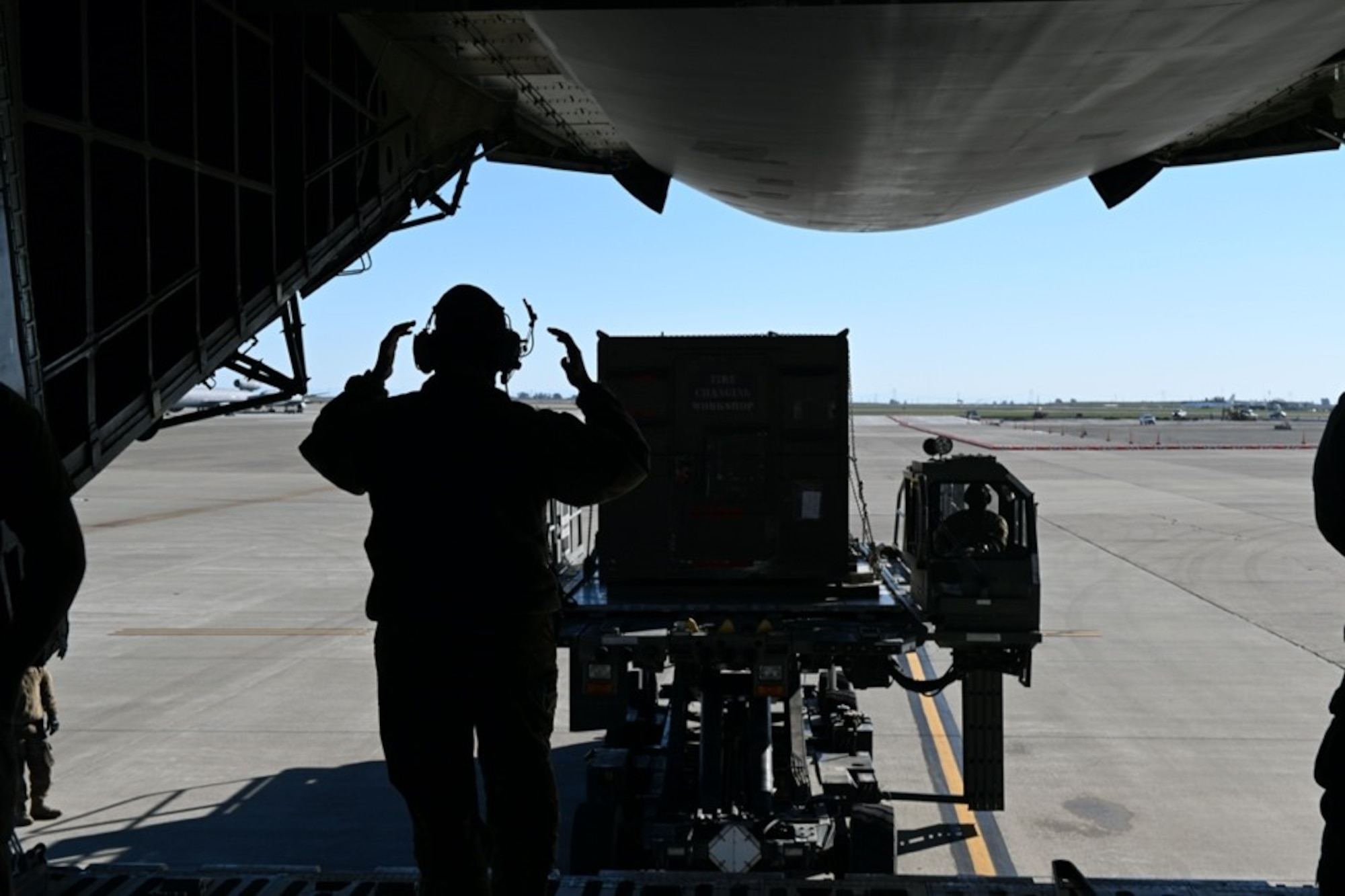 An Airman in a uniform and headset taxis in cargo into the gaping maw of a C-5M Super Galaxy