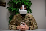 A participant in a virtual reality suicide prevention training pilot program sits while wearing a virtual reality headset and holding a virtual reality controller.