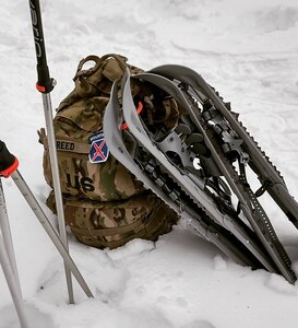 Army backpack with 10th Mountain Patch sits in the snow with snowshoes lying on top.