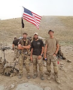 Three men stand with equipment on a hill