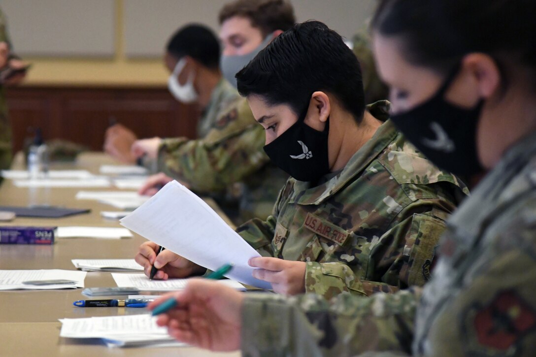 Four service members sit next to one another at tables to fill out paperwork; each is wearing a face mask.