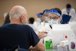 Petty Officer 3rd Class Michael A. Torrent conducts a pre-screening questionnaire prior to administering the COVID-19 vaccine as part of Operation Warp Speed at Walter Reed National Military Medical Center Jan. 14.