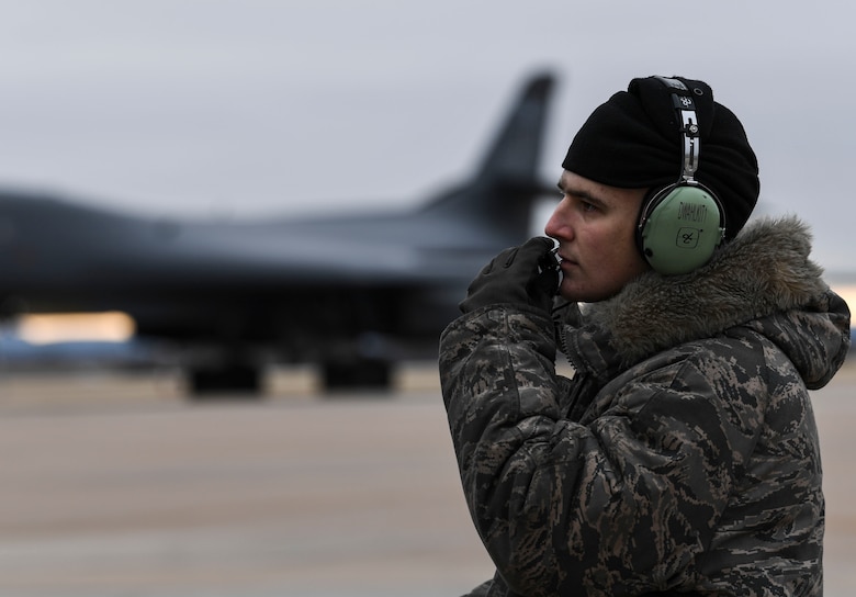 A crew chief wearing cold weather gear speaks into a headset.