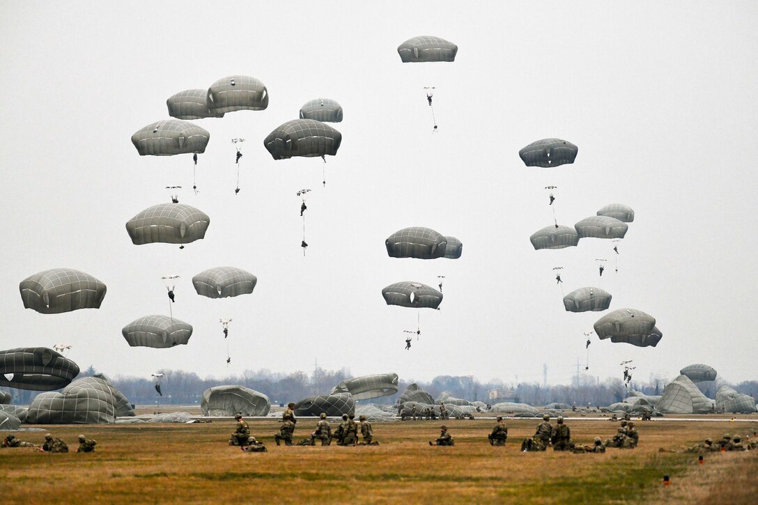 U.S. and Italian troops freefall with parachutes in a field.