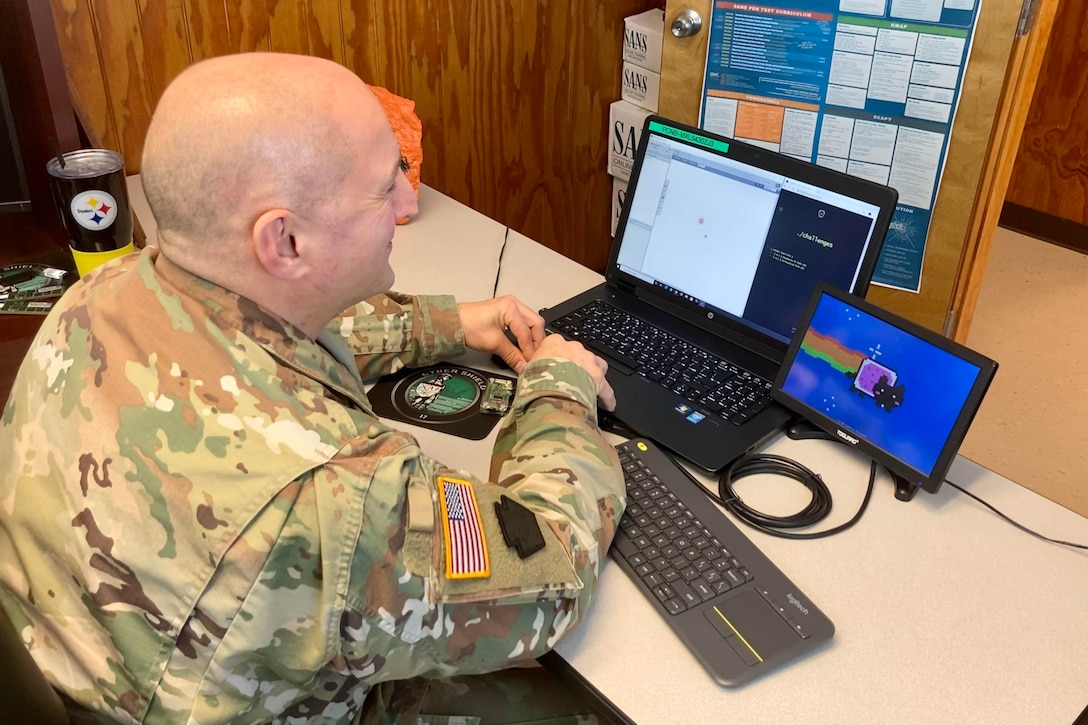 A man in a uniform types on a laptop.