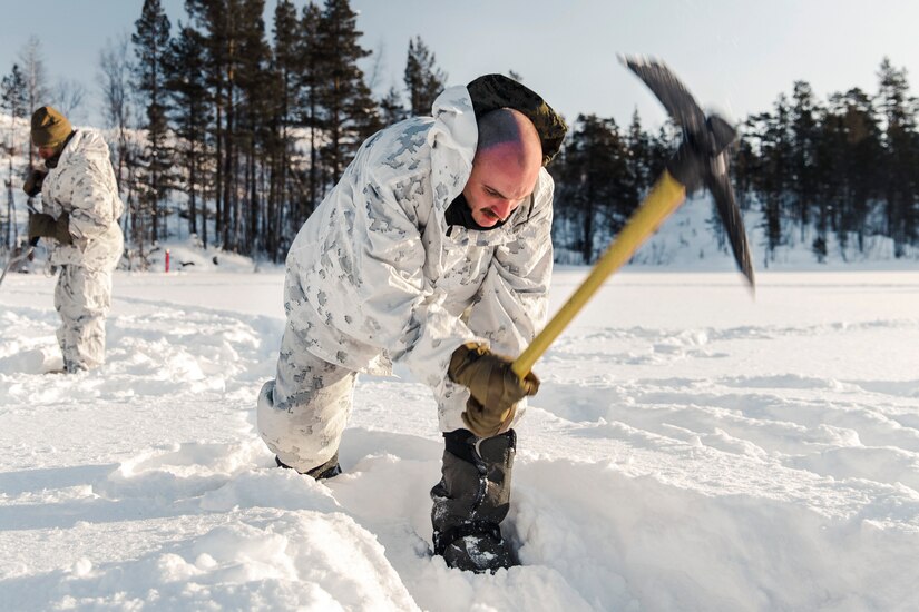 A Marine uses a tool to break ice.