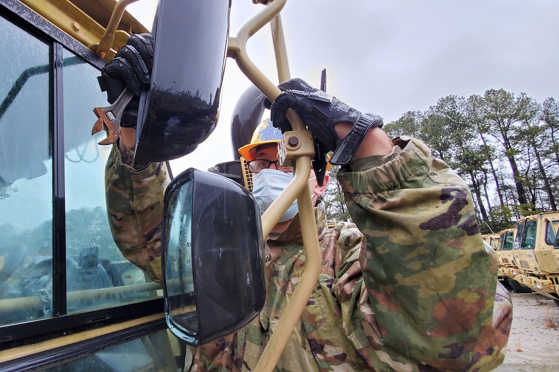 A soldier adjusts a part on the exterior of a vehicle.