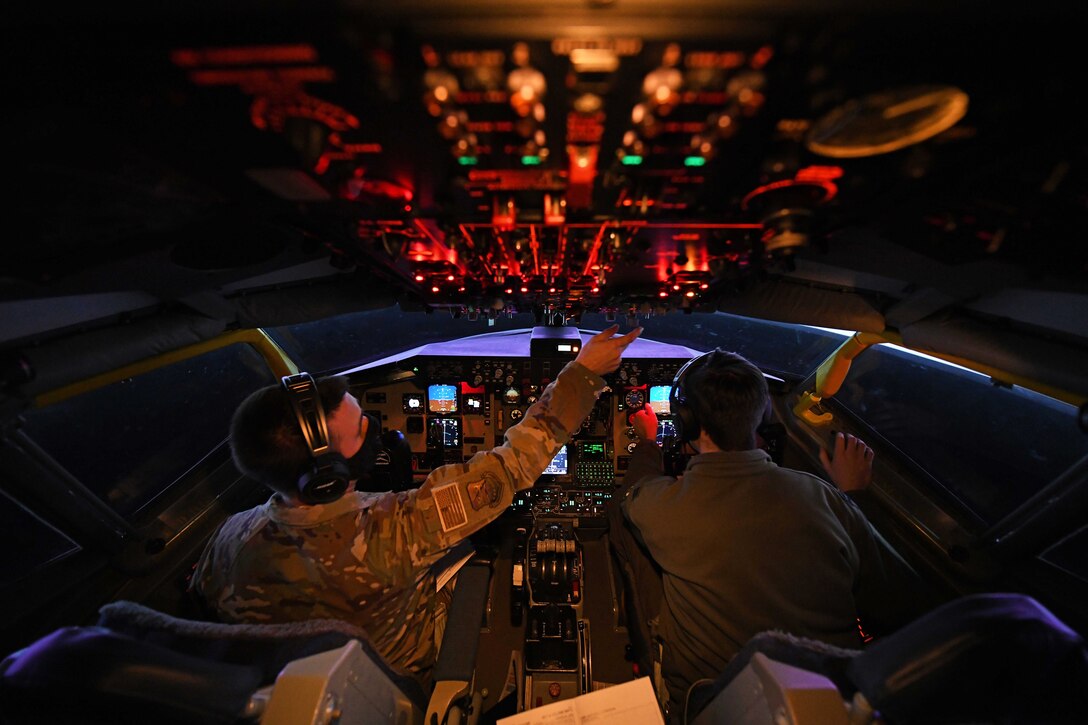 Two airmen prep the controls in a cockpit.