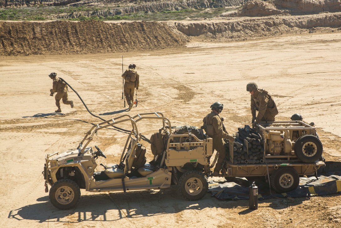 Marines work on and around a vehicle on sandy soil.