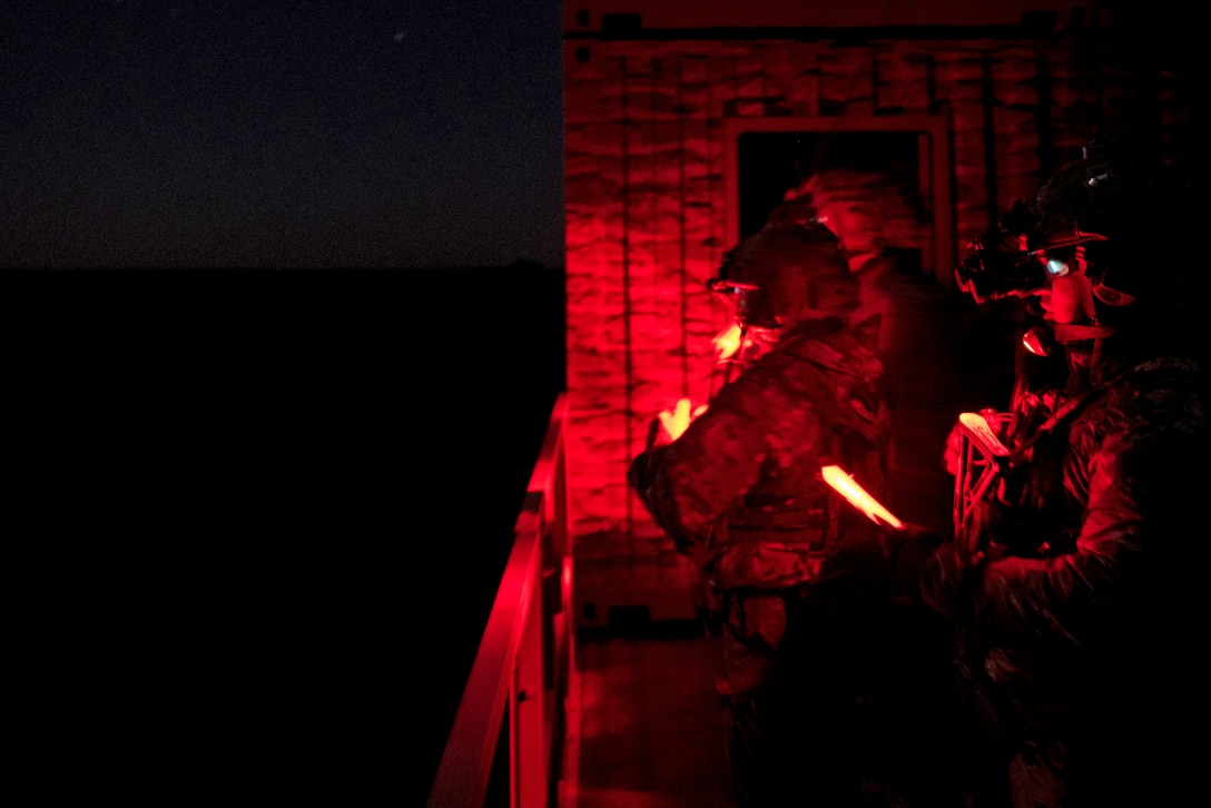 Airmen are seen in red light while holding lights during a night exercise.
