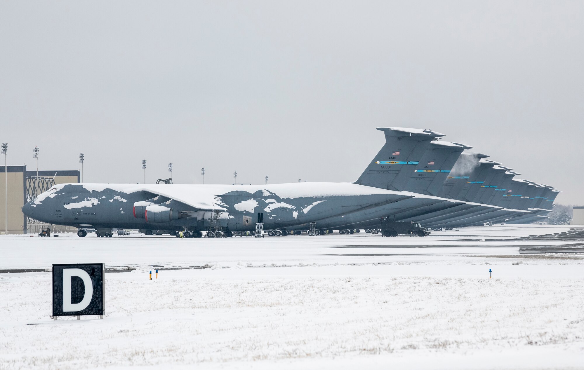 Snow-covered C-5M Super Galaxy aircraft sit on the flight line at Dover Air Force Base, Delaware, Feb. 11, 2021. As snow fell, the base continued normal operations and prepared for additional snowfall. (U.S. Air Force photo by Senior Airman Christopher Quail)