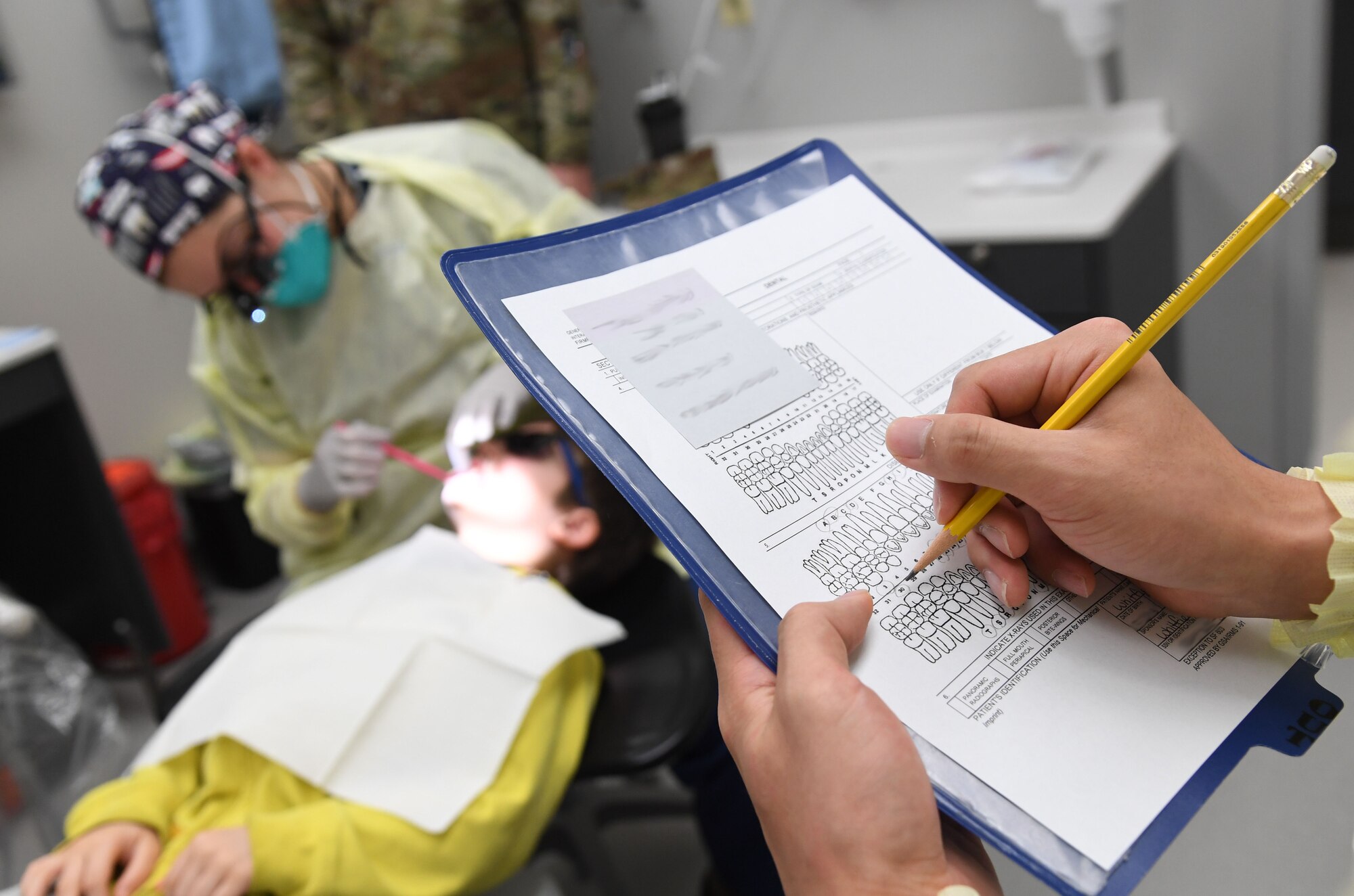 U.S. Air Force Airman 1st Class Sunghoon Kwon, 81st Dental Squadron dental technician, labels teeth findings on a chart as Capt. (Dr.) Emily Doe, 81st DS general dentist, conducts a dental exam on Tobias Whitfield, son of Airman 1st Class James Whitfield, 85th Engineering Installation Squadron radio frequency transmissions technician, during the 10th Annual Give Kids a Smile Day at the dental clinic inside the Keesler Medical Center at Keesler Air Force Base, Mississippi, Feb. 17, 2021. The event was held in recognition of National Children's Dental Health Month and included free dental exams and cleanings for children ages 1-12. (U.S. Air Force photo by Kemberly Groue)