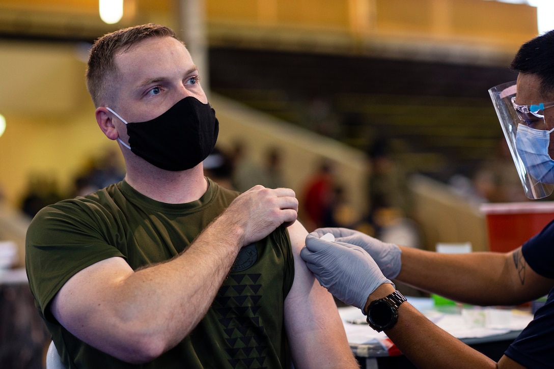 A Marine wearing a face mask receives a COVID-19 vaccine from a medical tech wearing a face mask and gloves.