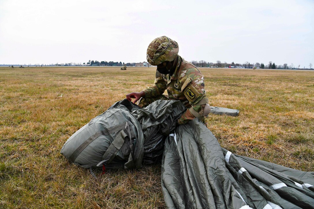 A soldier gathers parachute equipment in a field.