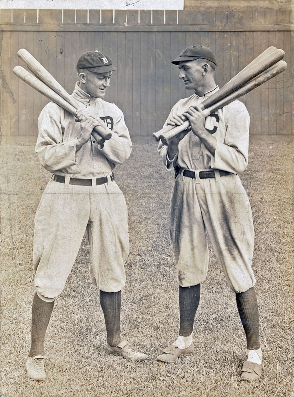Two baseball players hold bats over their shoulders.