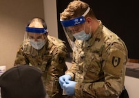 U.S. Army Spc. Zachary Burton, left, and Spc. Cody Taylor, right, both with the 531st Hospital Center, Fort Campbell, Ky., prepare a COVID-19 vaccine for a patient at First Baptist Church of Lincoln Gardens in Somerset, N.J., Feb. 17, 2021.