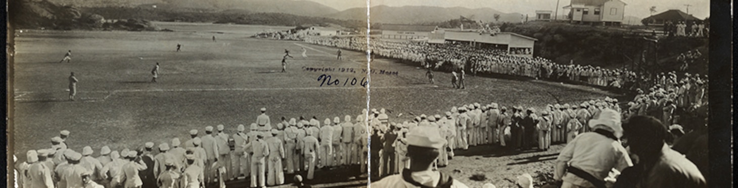 Black and white photo of baseball field with players lined along the sidelines