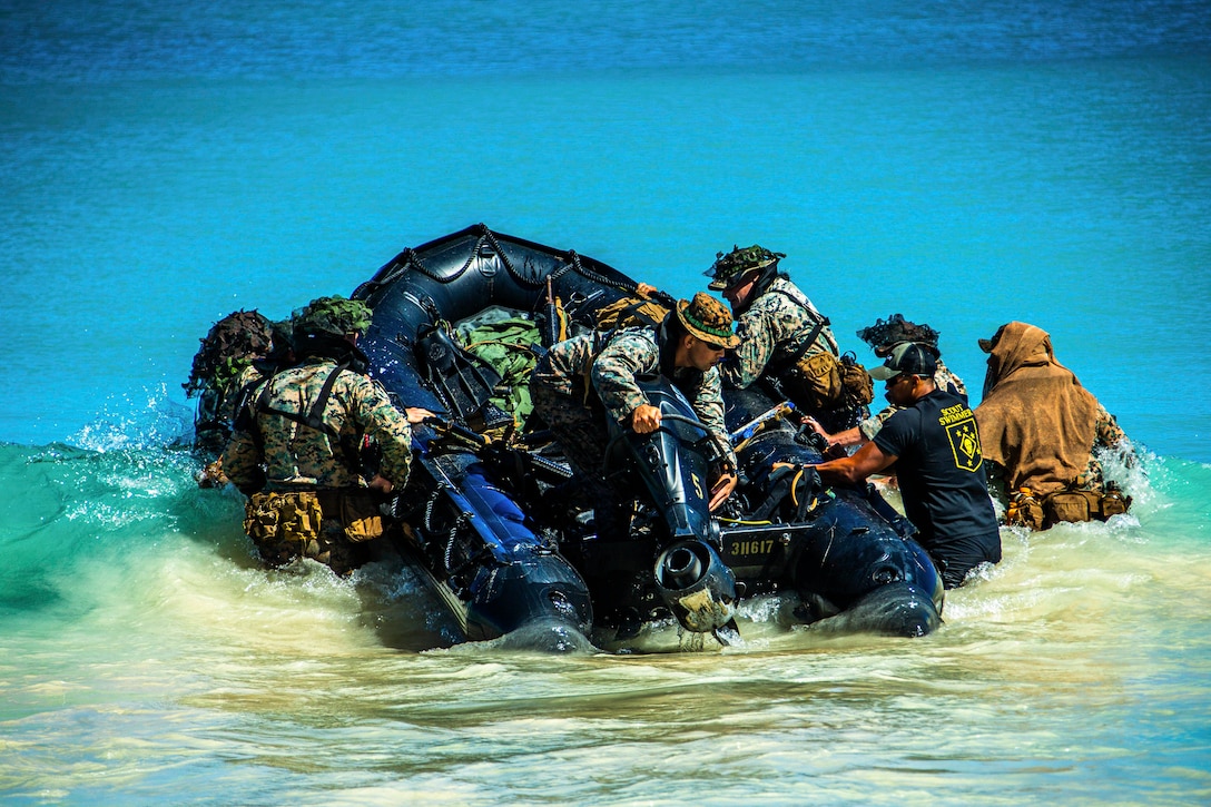 Marines bring a small rubber craft into a body of water.