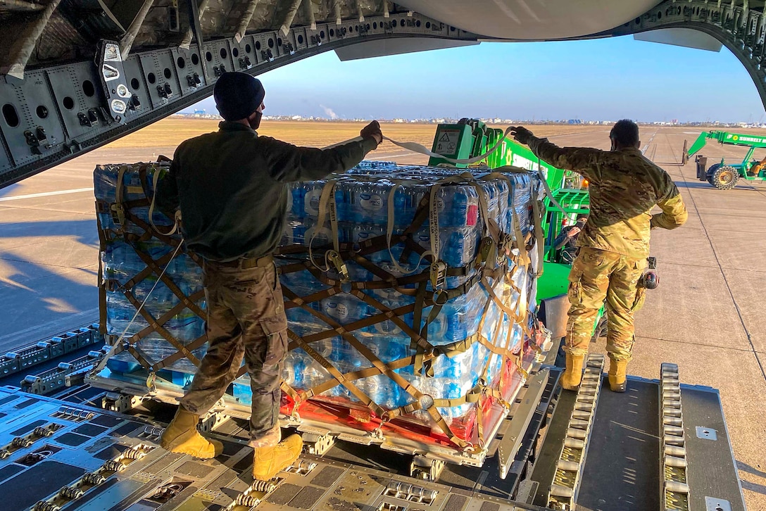 Two airmen move a pallet of bottled water at the back of an aircraft.