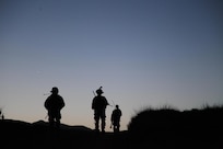 Three soldiers patrol a grassy landscape at dawn