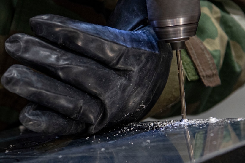 Photo of an Airman drilling rivets on sheet metal.