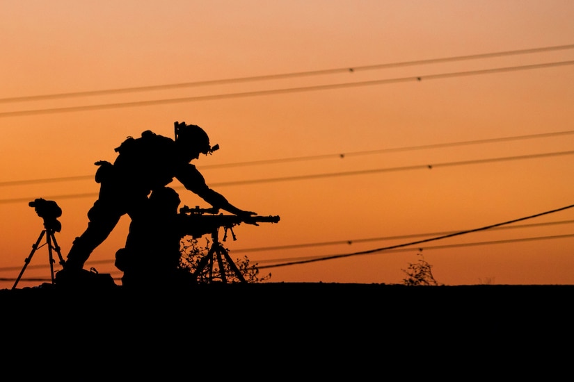 A soldier adjusts a weapon in silhouette.