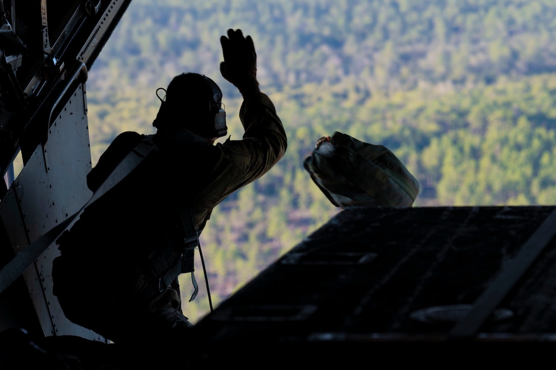 An airman throws a sack out the back of an aircraft.