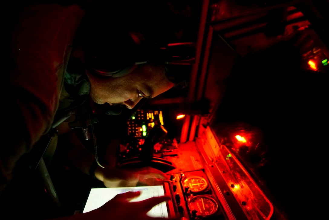 An airman in orange light handles controls inside an aircraft.