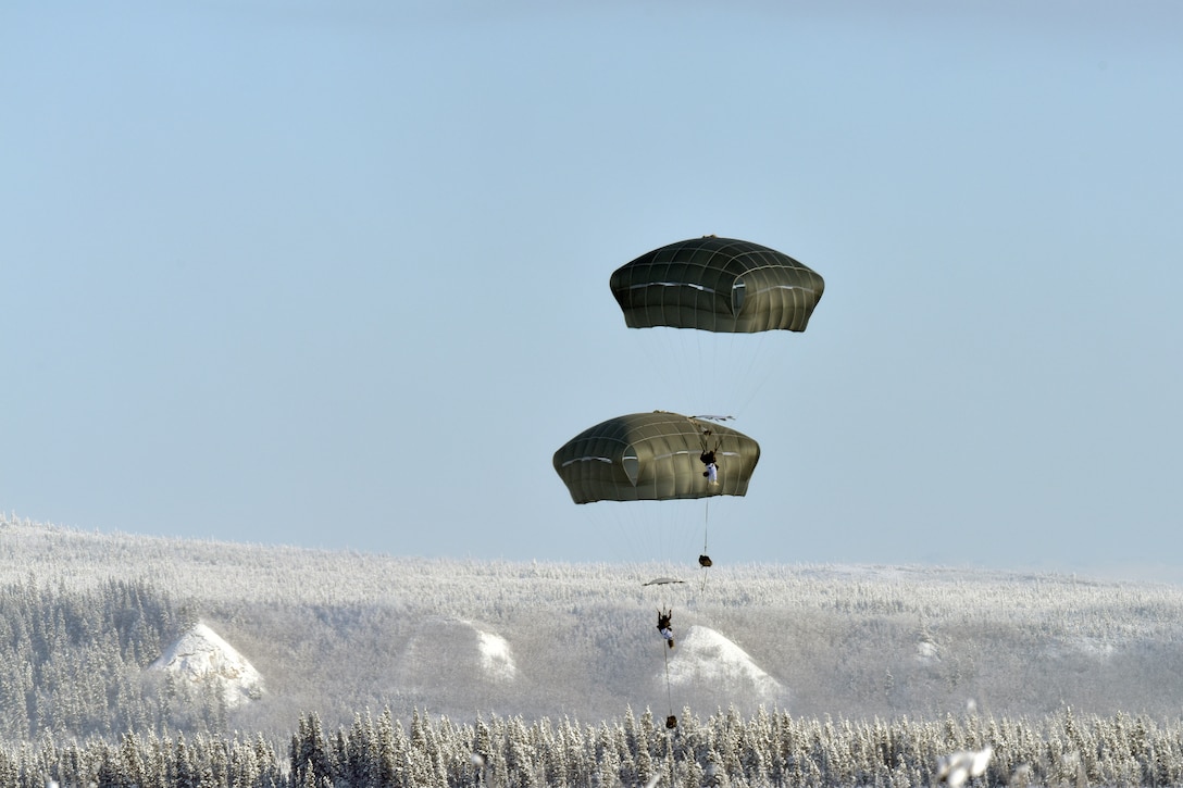 Two paratroopers descend over wintry terrain.