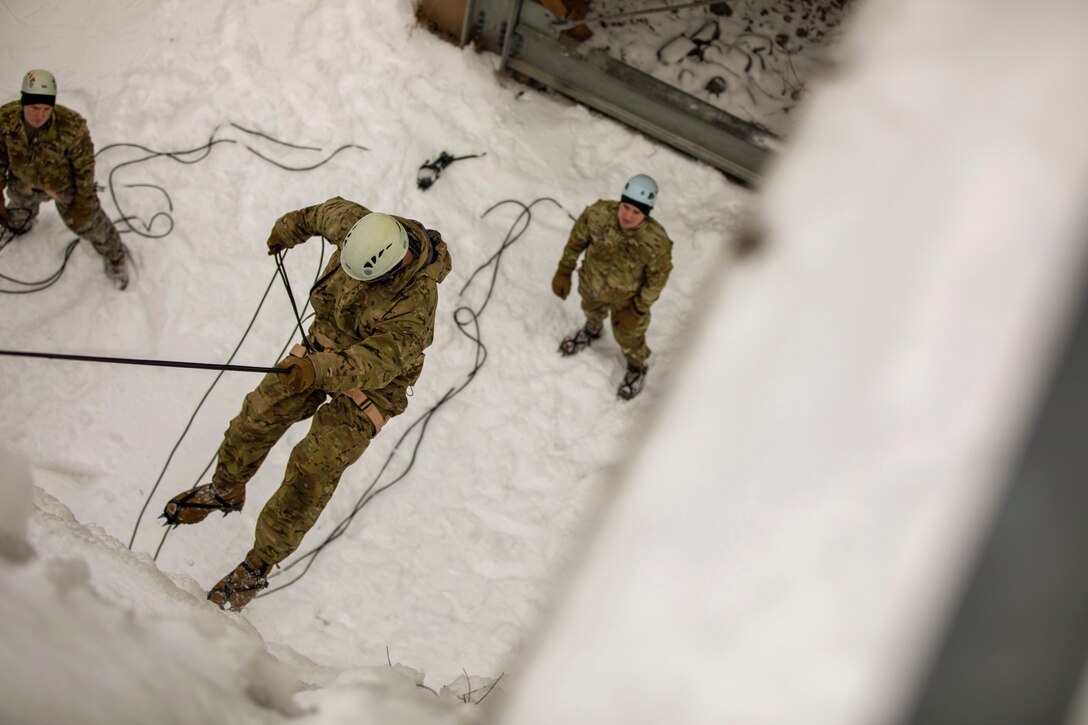 A soldier rappels down an icy wall.