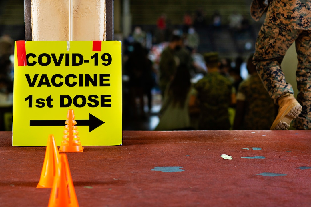 A sign on the floor points the way to COVID-19 vaccines as a service member walks down some stairs.