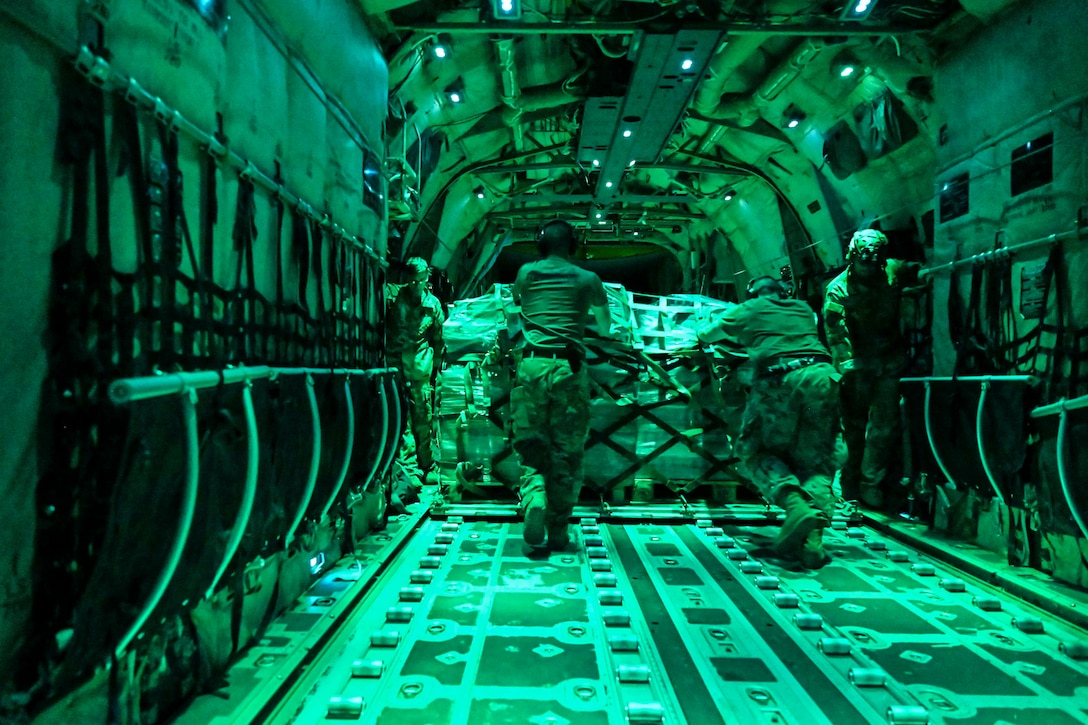 Airmen illuminated by green light move a pallet inside an aircraft.