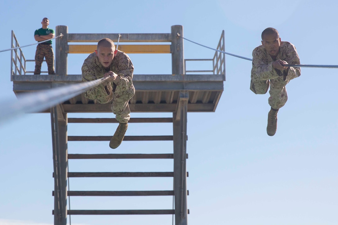 Two Marines Corps recruits move across a rope obstacle.