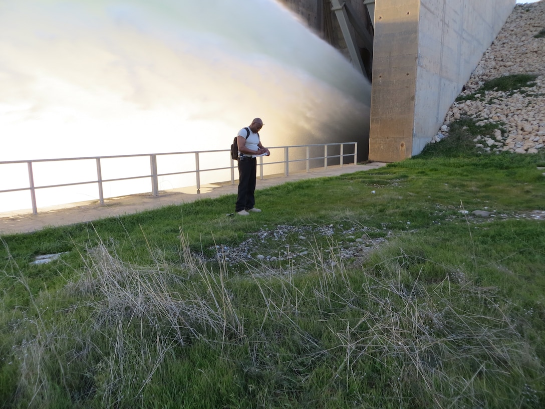 man standing in front of an active dam spillway